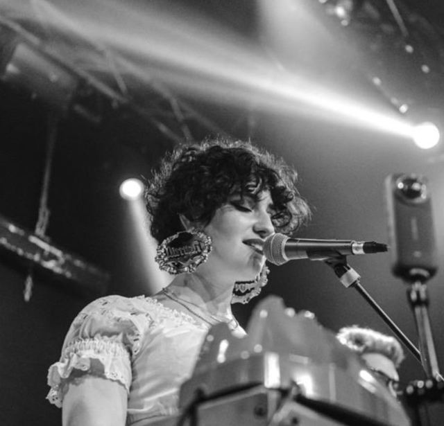 Ritratto: una ragazza canta al microfono su un palco.