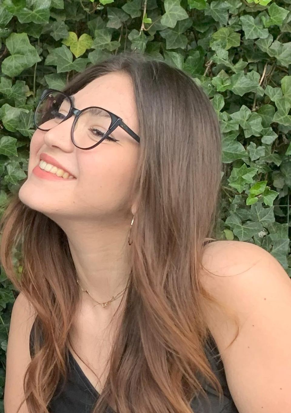 Ritratto: una ragazza con gli occhiali sorride davanti a una siepe d’edera.