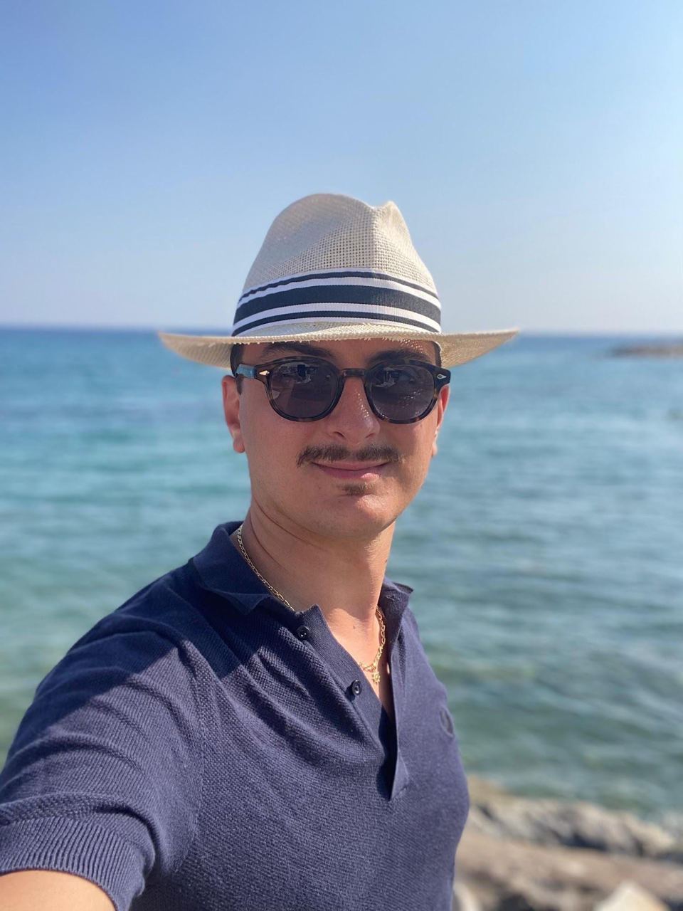 Ritratto: un ragazzo con cappello di paglia e occhiali da sole, in riva al mare.