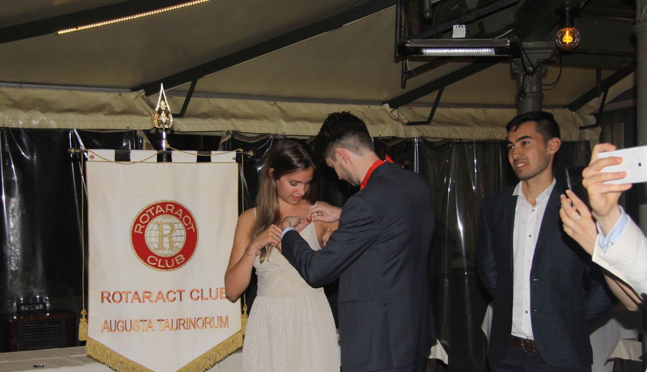 Foto d’archivio: durante una serata un ragazzo appunta una spilla sull’abito di una ragazza, davanti a un gagliardetto Rotaract.