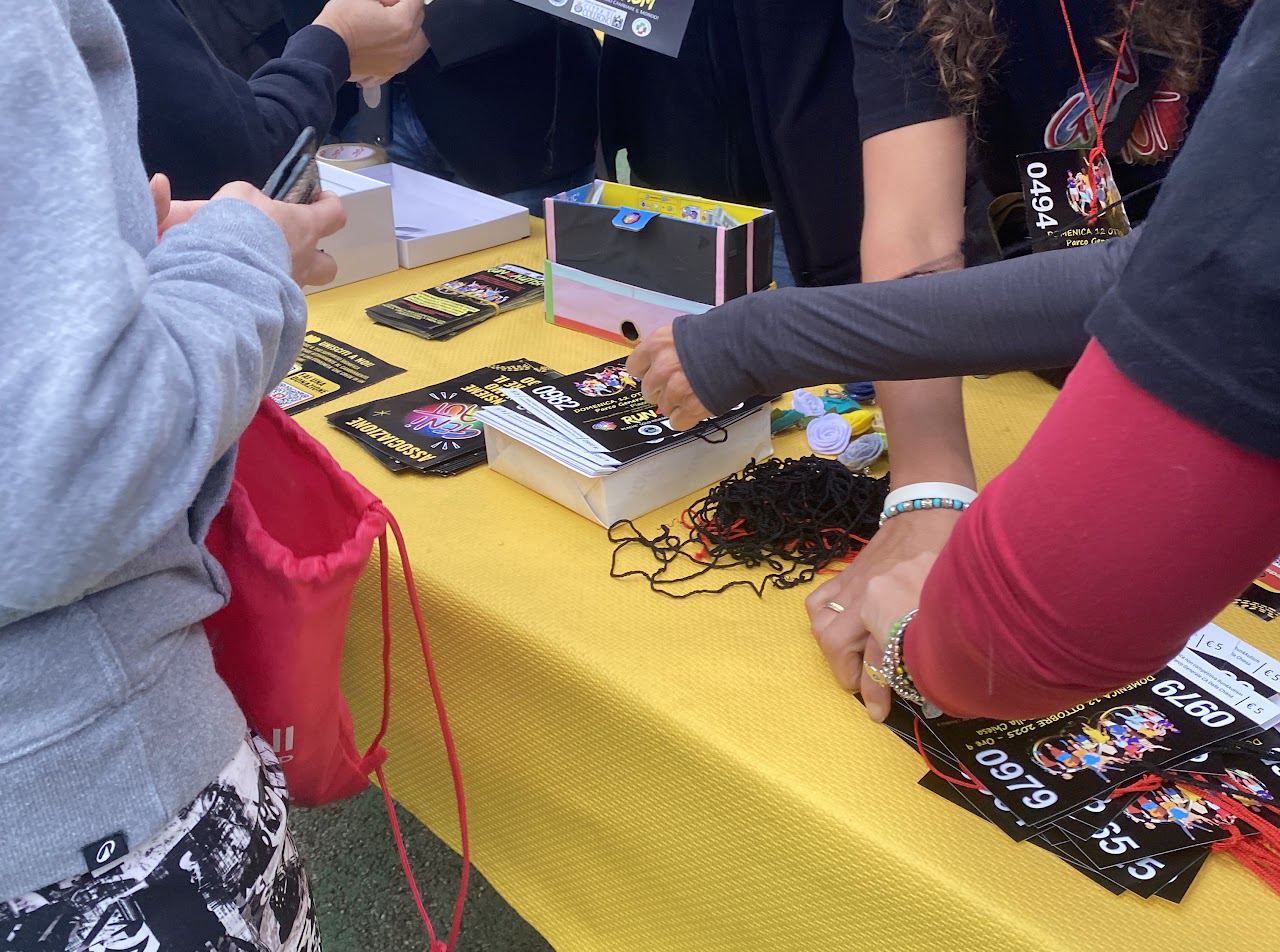 Il banchetto della Run4Autism: mani che distribuiscono i biglietti della corsa solidale su una tovaglia gialla.