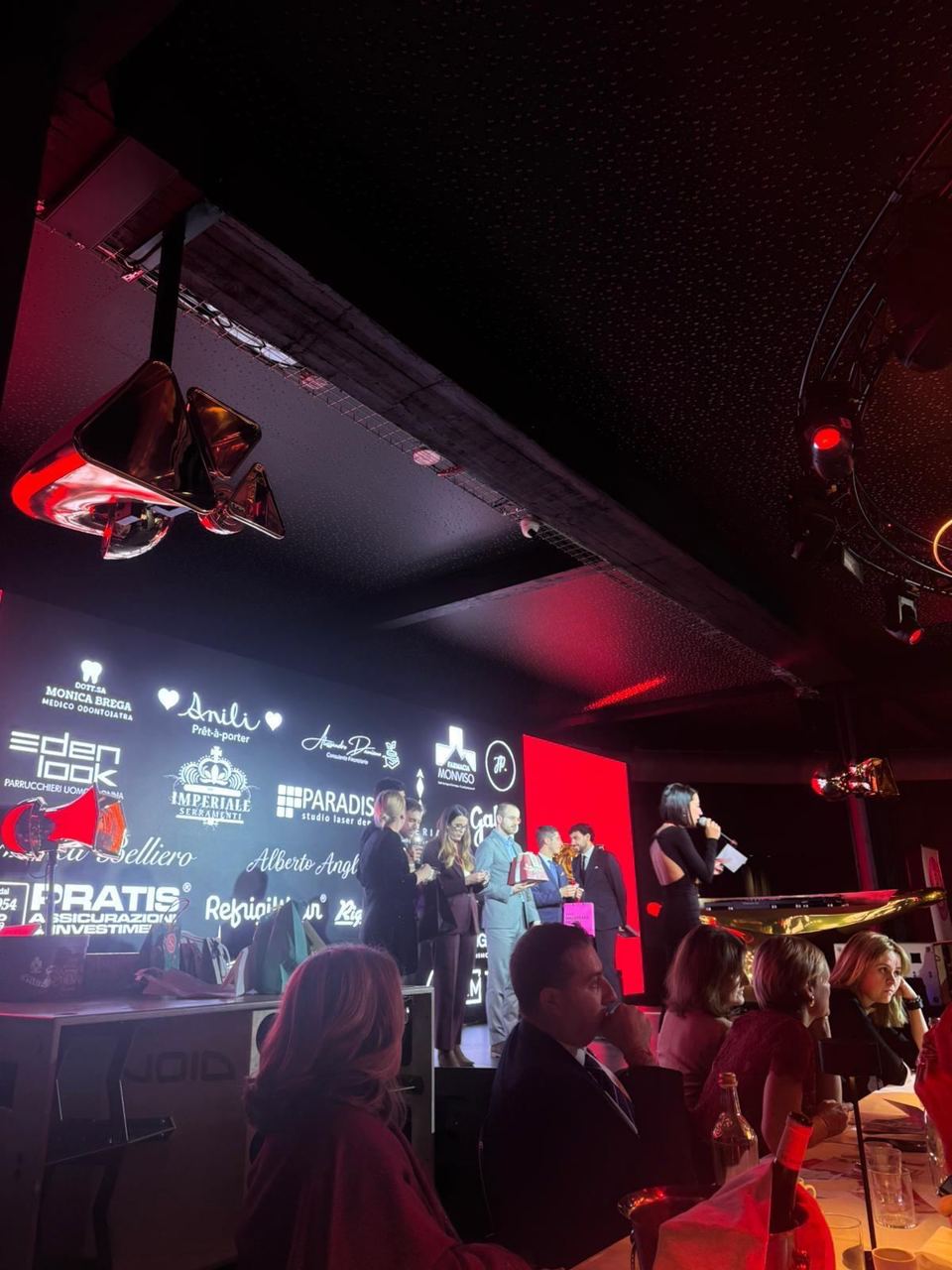 Il palco durante la serata, con i nomi degli sponsor sullo schermo e gli ospiti ai tavoli.