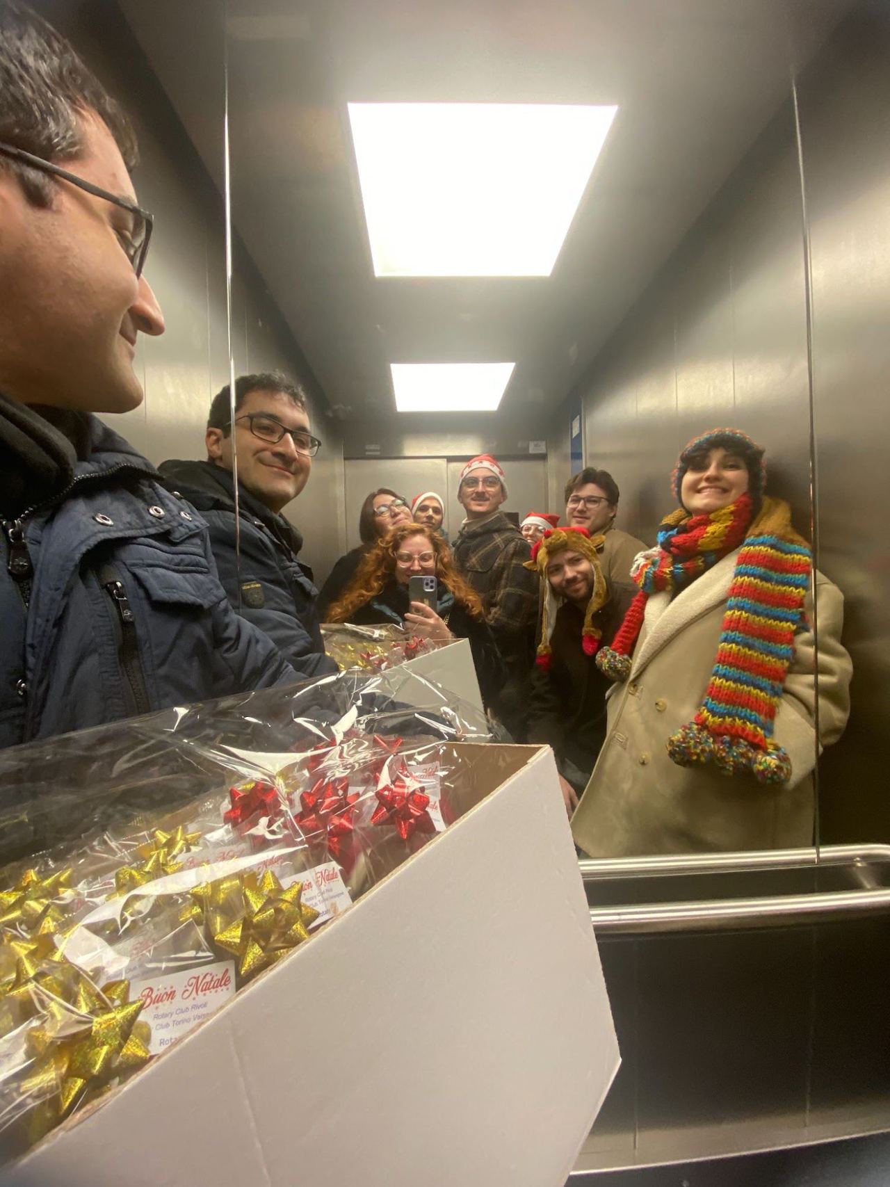 Un gruppo di ragazzi in ascensore con una scatola piena di doni incartati.