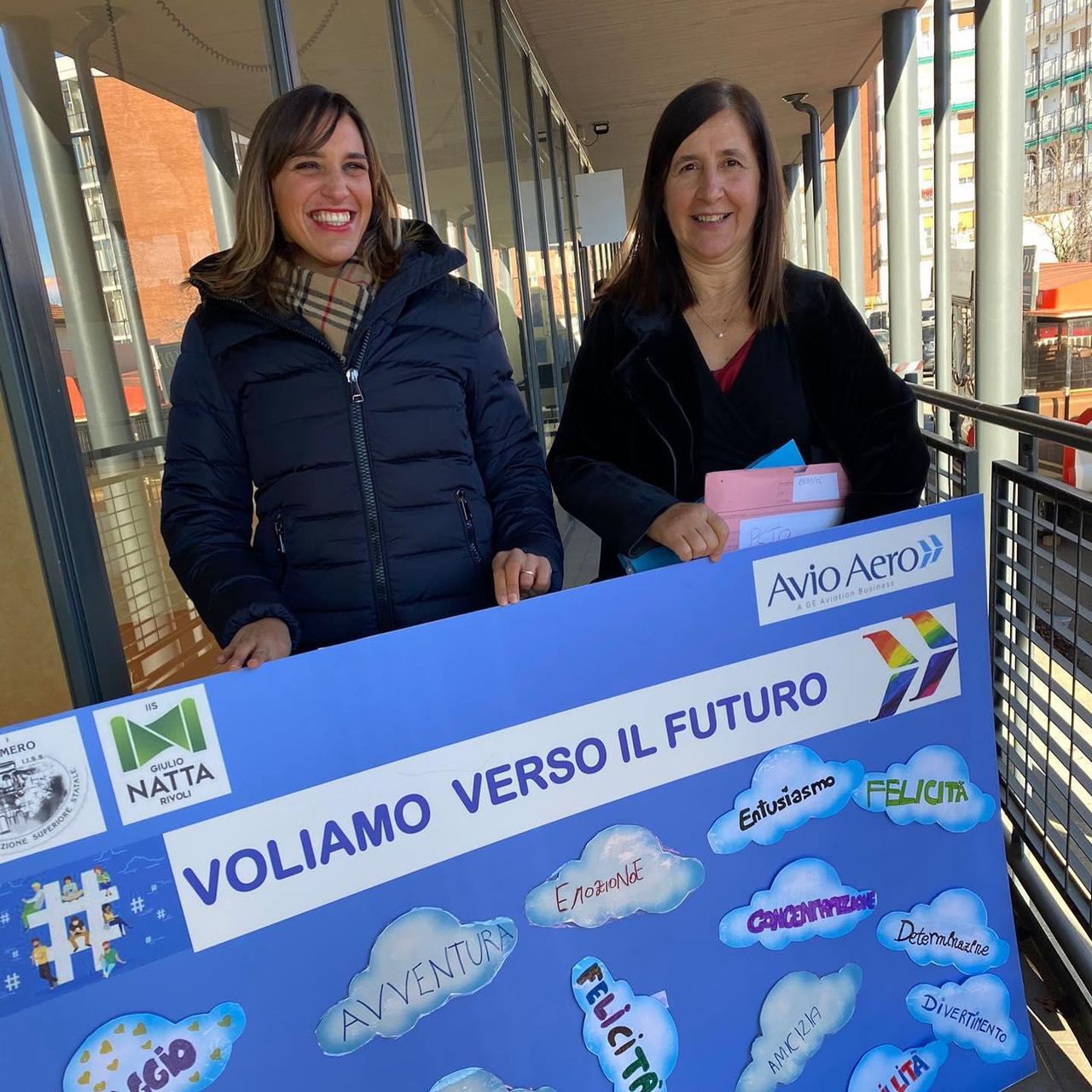Due partecipanti sorridenti reggono il cartellone «Voliamo verso il futuro» con i loghi di Avio Aero e dell’IIS Giulio Natta.