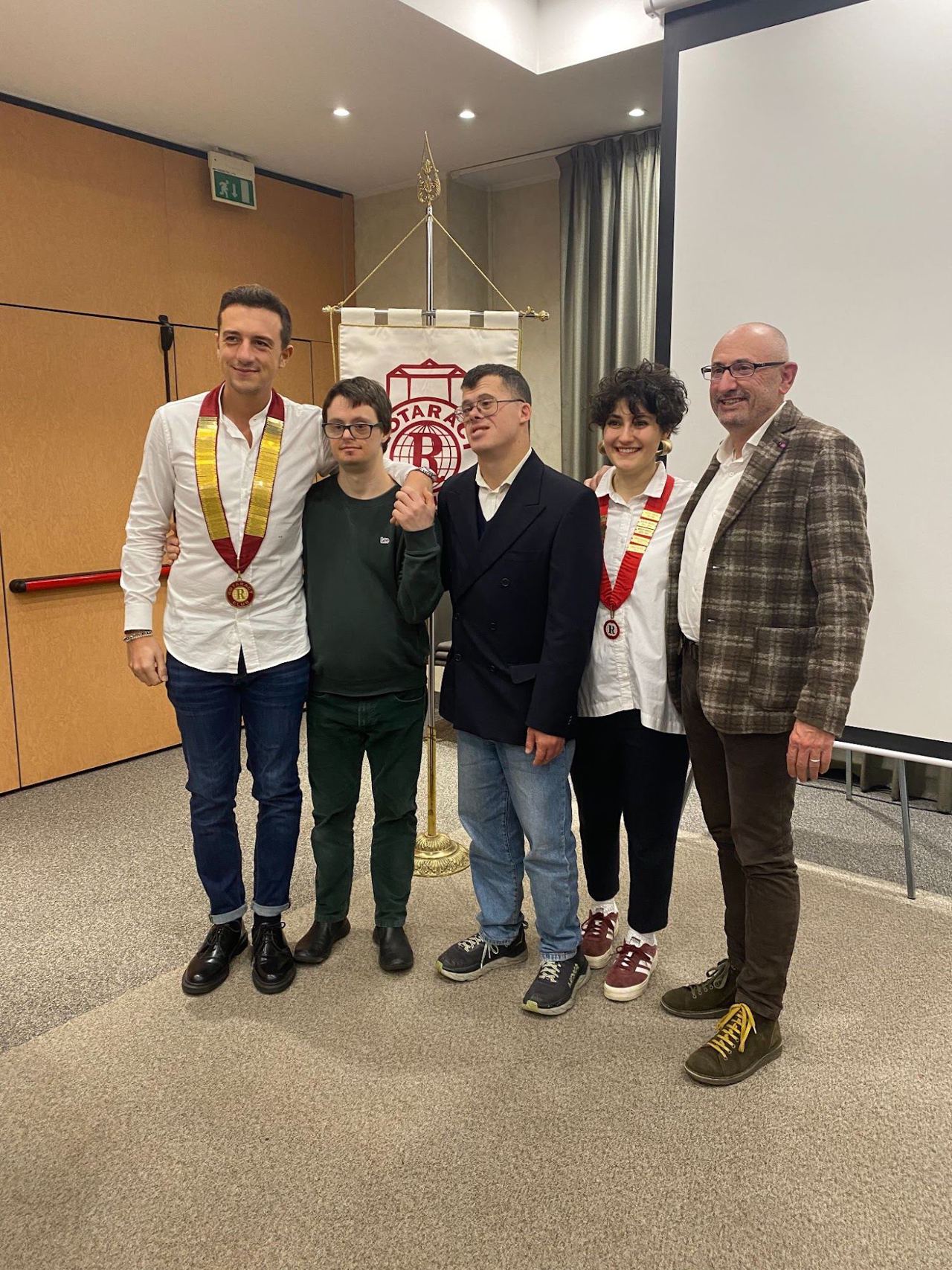 Cinque persone in posa davanti allo stendardo del Rotaract Club Rivoli, due delle quali con il collare del club.
