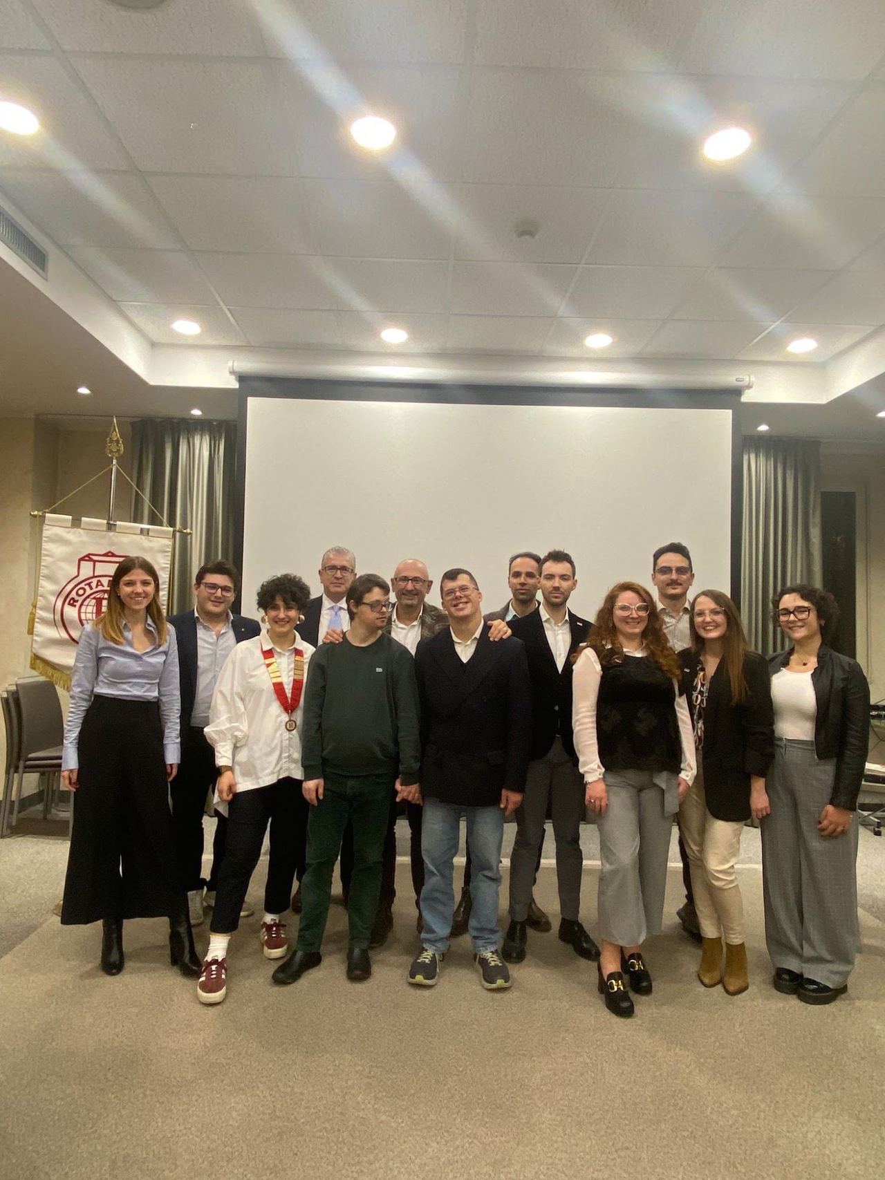 Foto di gruppo in una sala, davanti allo schermo e allo stendardo del Rotaract.