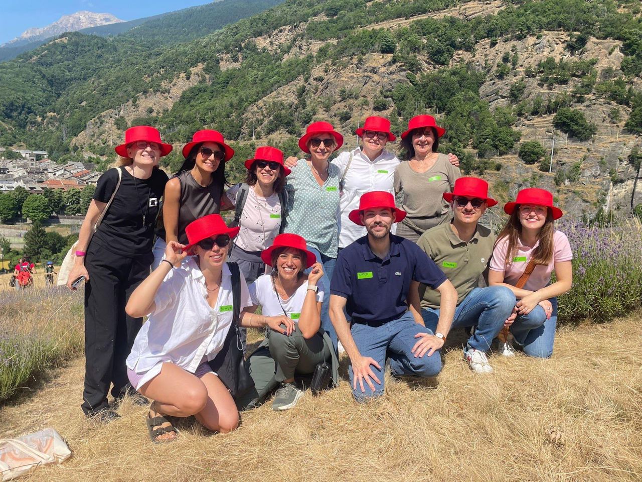 Ragazze e ragazzi con cappelli rossi in posa sul prato del Forte di Exilles, con le montagne alle spalle.